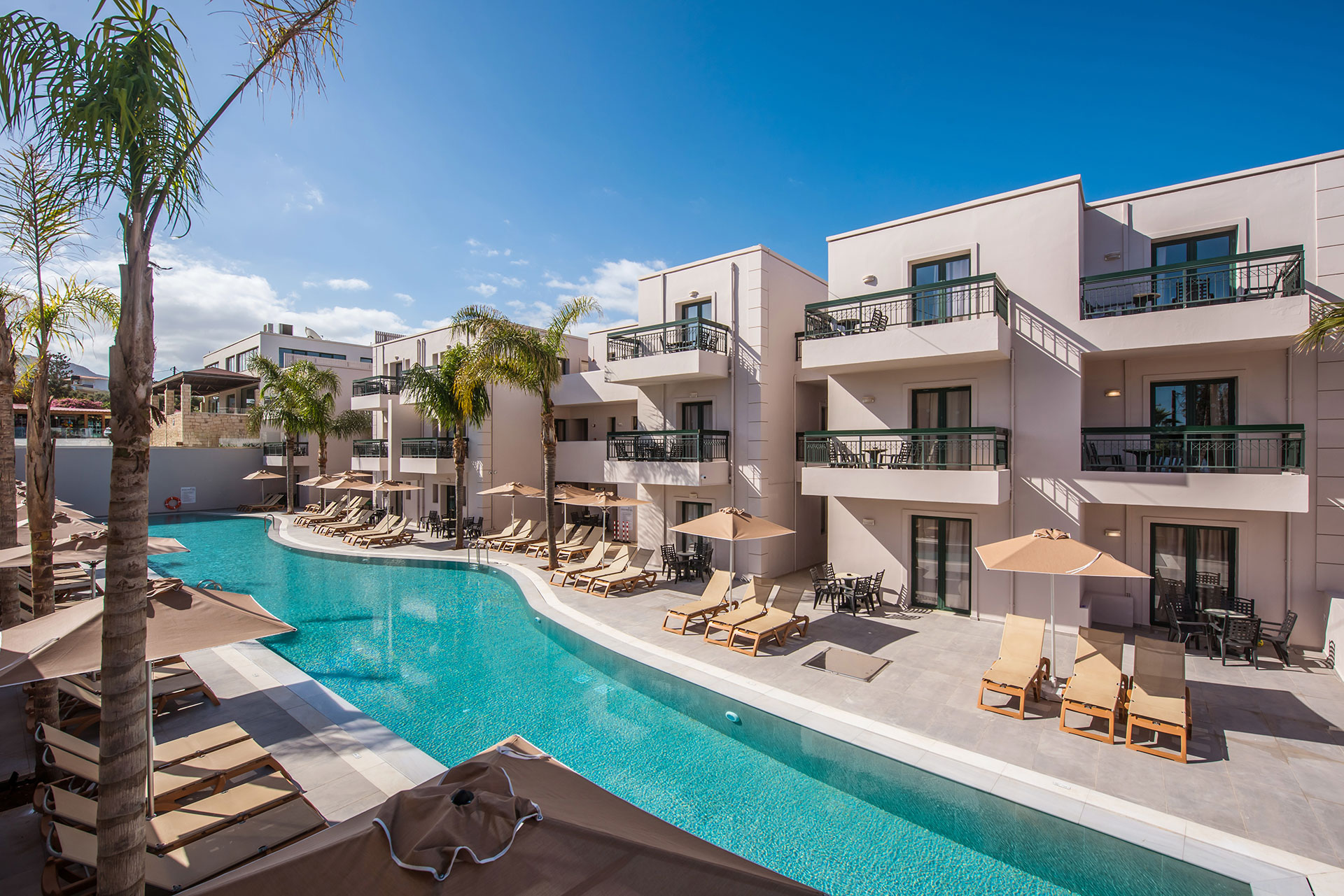 Curved outdoor pool with palm trees, sun loungers and modern balconies at Gouves Water Park Holiday Resort